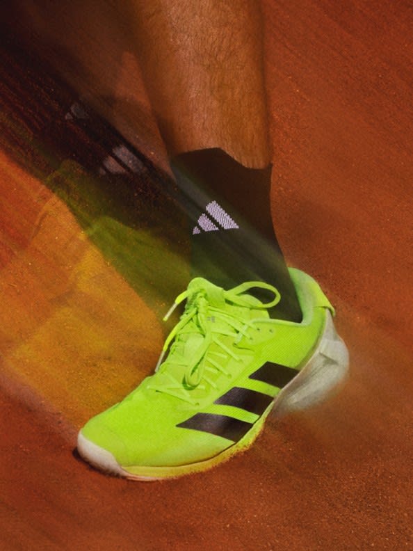 The image shows a pair of bright green and black athletic shoes on a wooden floor.