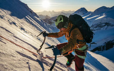 An alpinist is climbing the side of a snowy mountain wearing technical TERREX gear.