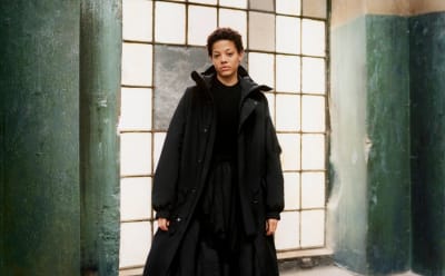 A model is pictured in front of a raw industrial window wearing a black Y-3 jacket.