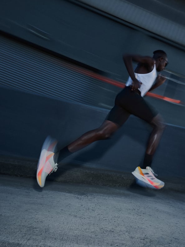 A man running on road, blurred in motion, wearing the Adizero Boston 12.