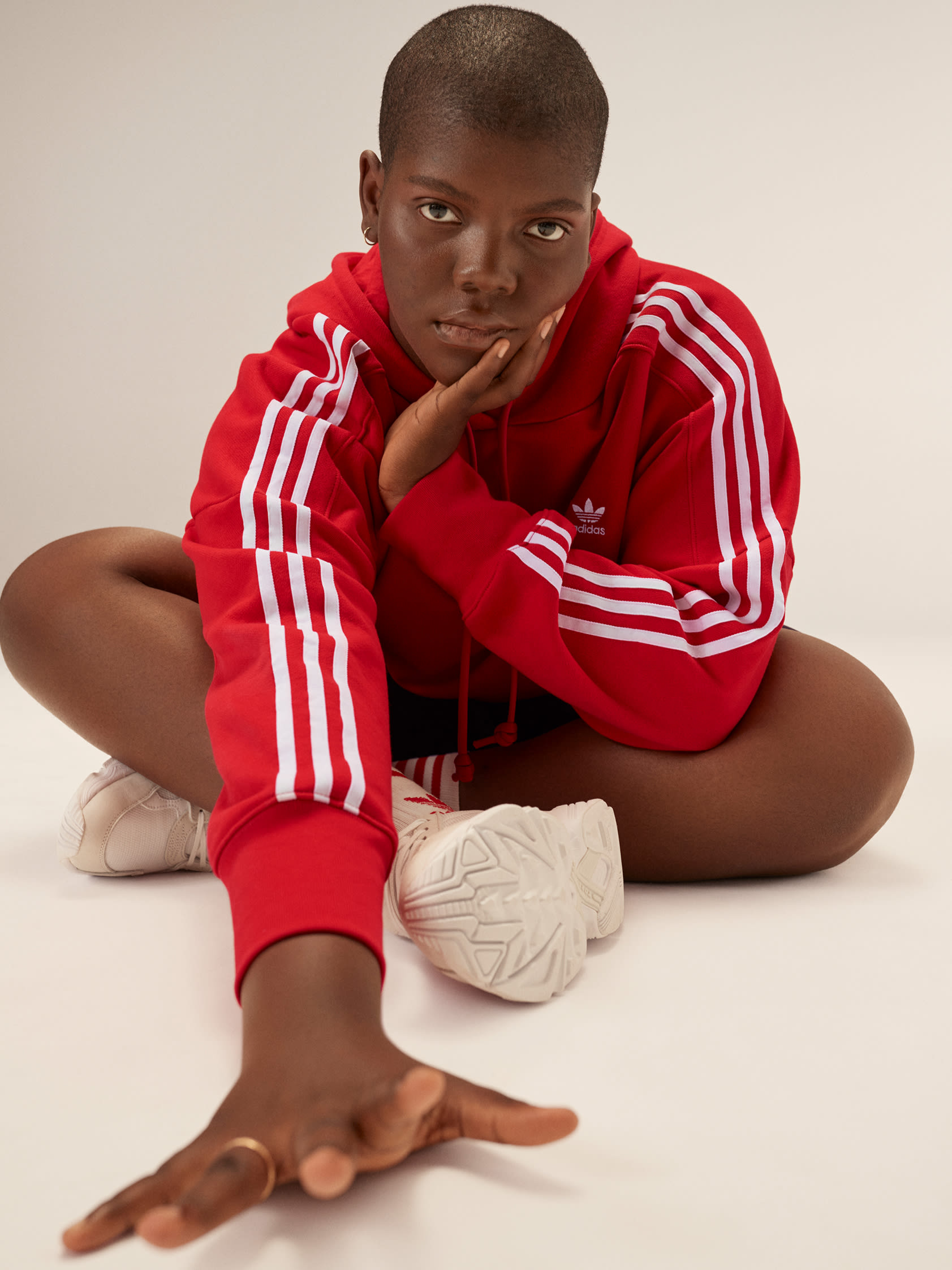 Stylish woman poses in red adicolor hoodie, black shorts