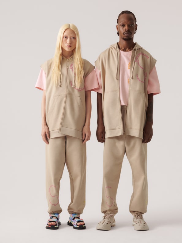 Two models standing, they wear the new sleeveless hoodie and sweat pants from the SS23 adidas by Stella McCartney gender-neutral loungewear drop. Crafted from 100% organic cotton.