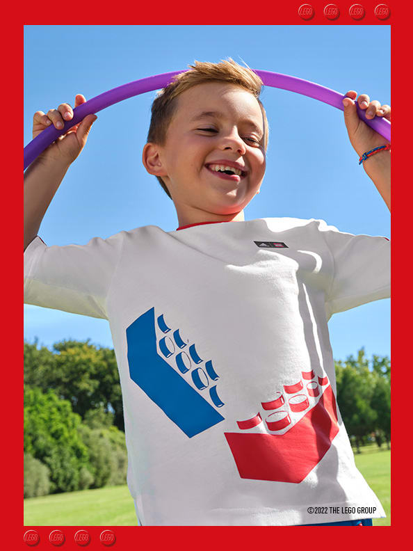 Young smiling boy playing with hula hoop in a park wearing a white adidas LEGO t-shirt