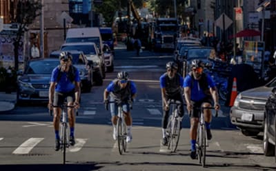 FOUR PEOPLE CYCLING NEXT TO EACH OTHER DOWN A STREET