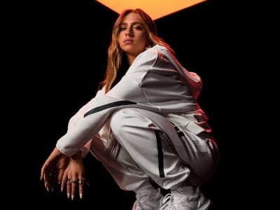Singer Tate McRae wearing a white adidas tracksuit top and bottoms in a crouched position.