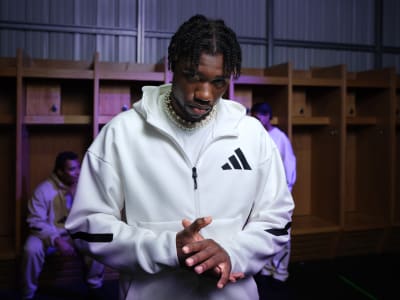 Sprinter Noah Lyles standing in a locker room wearing white adidas tracksuit top.