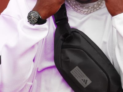 A close up of a person with a hood up wearing a black adidas cross body bag.