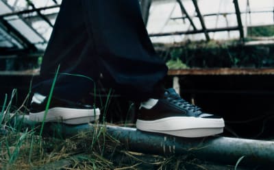 A black and white Y-3 sneaker balances on a steel pipe in nature.