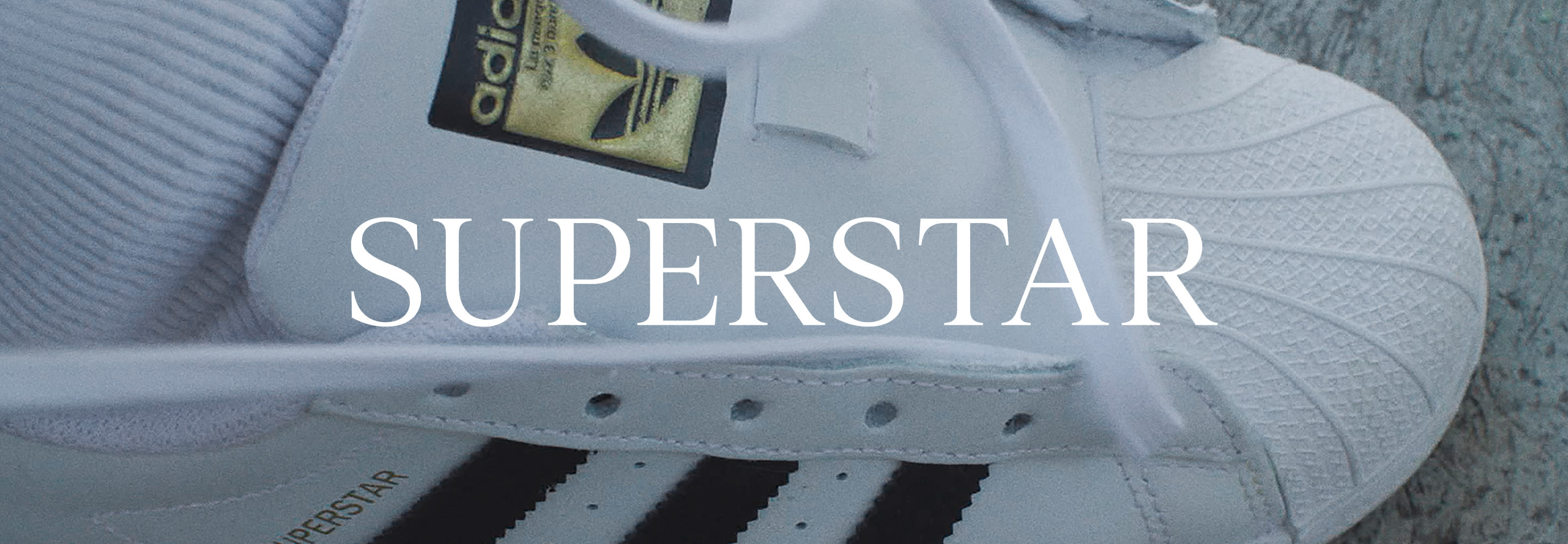 A pair of adidas Originals Superstar shoes are photographed on the ground.