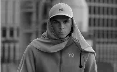 A upperbody photo of a man wearing white Y-3 apparel standing in front of a building.
