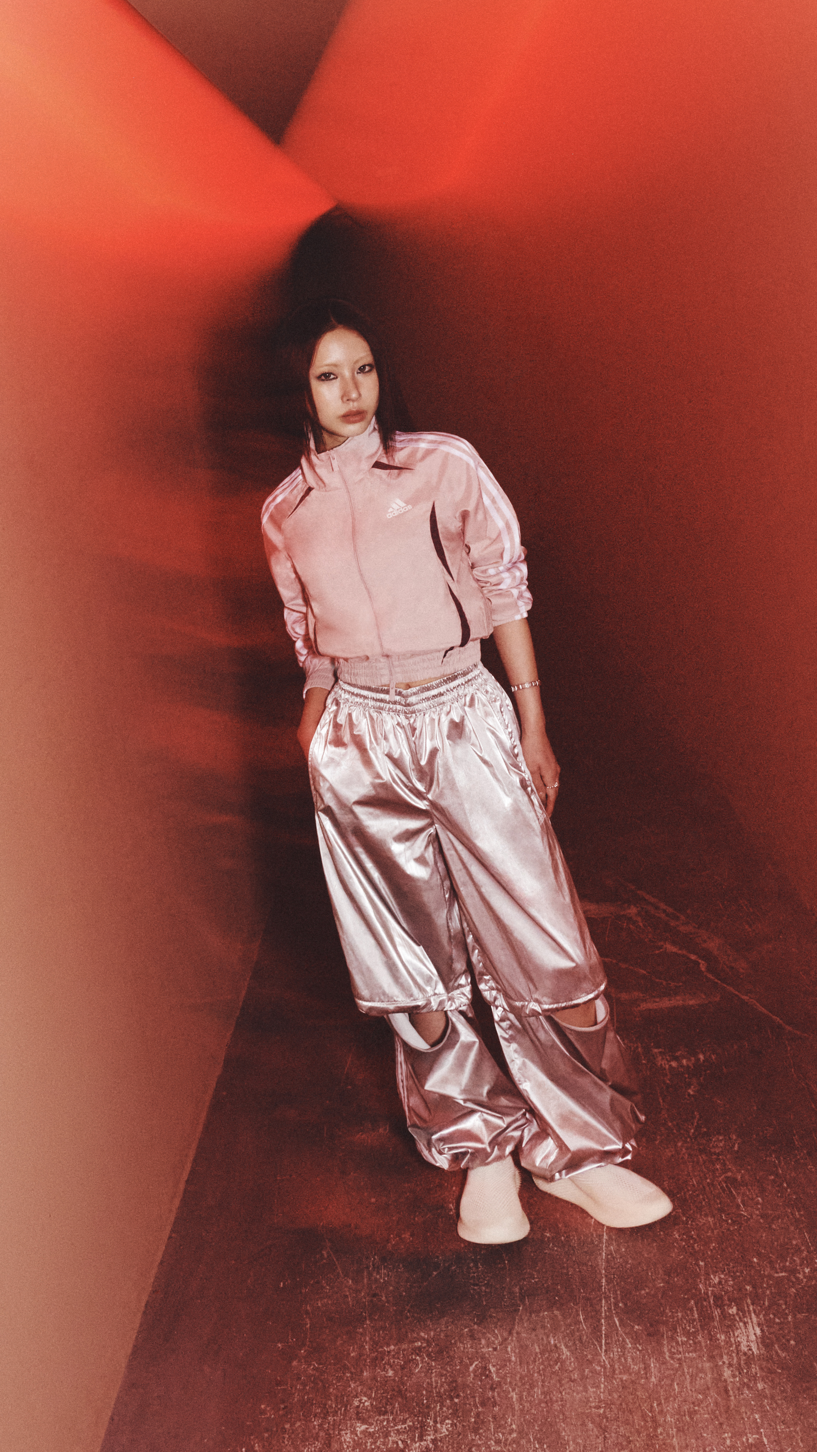 A person wearing a pink outfit stands in a dimly lit, reddish-orange environment.