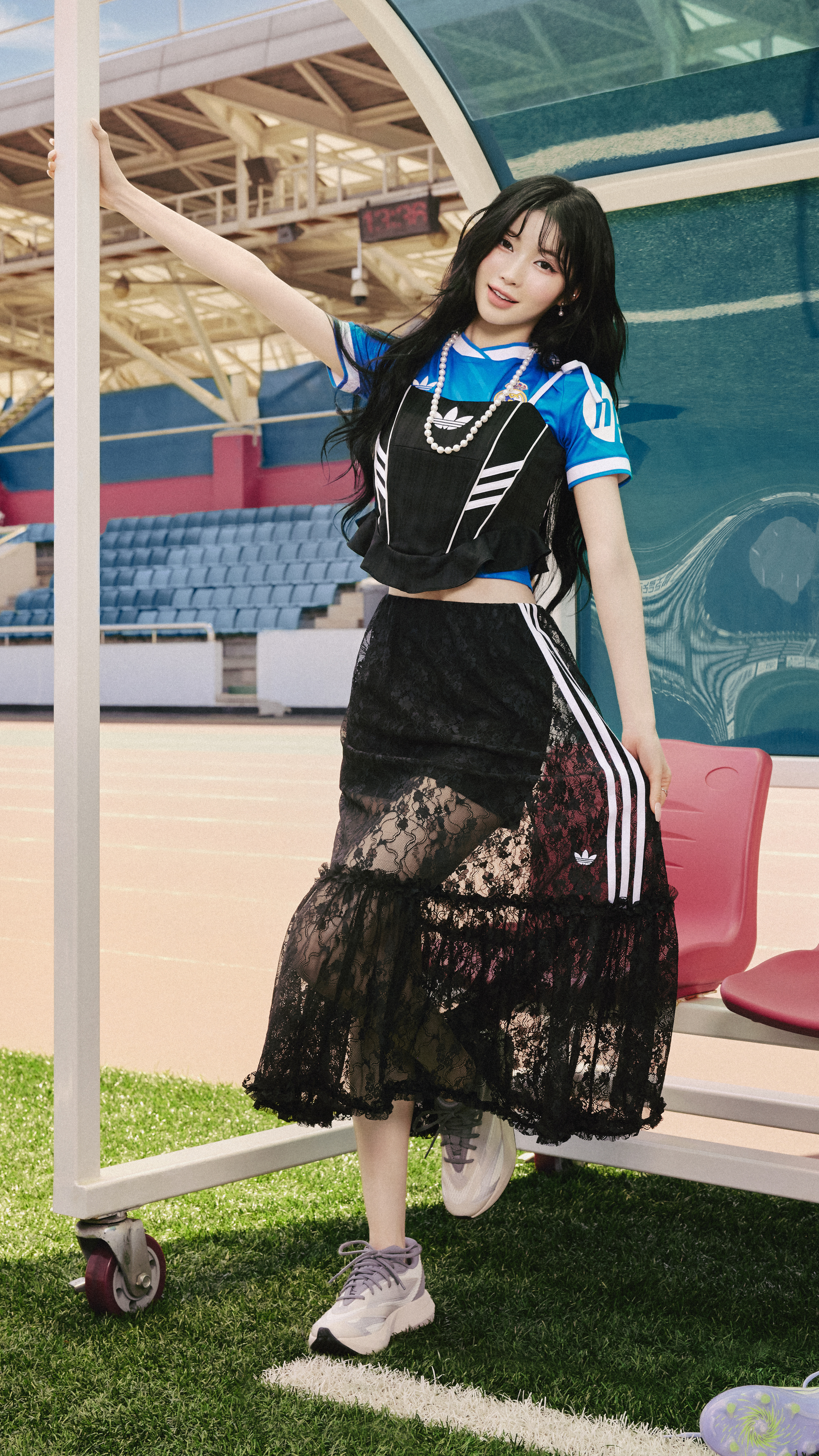A young woman in a black and blue athletic outfit stands on a grassy field in front of a sports stadium.