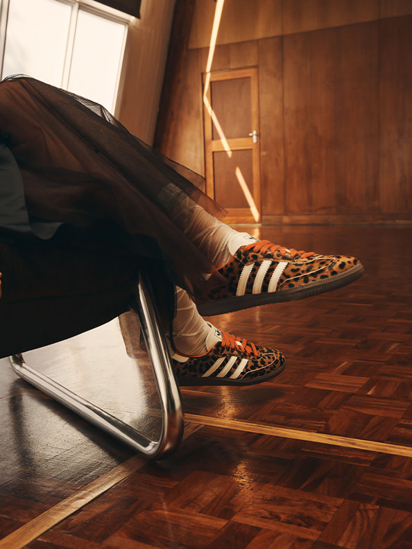 A pair of leopard-print sneakers rests on a wooden floor, with a mirror reflecting the scene in the background.