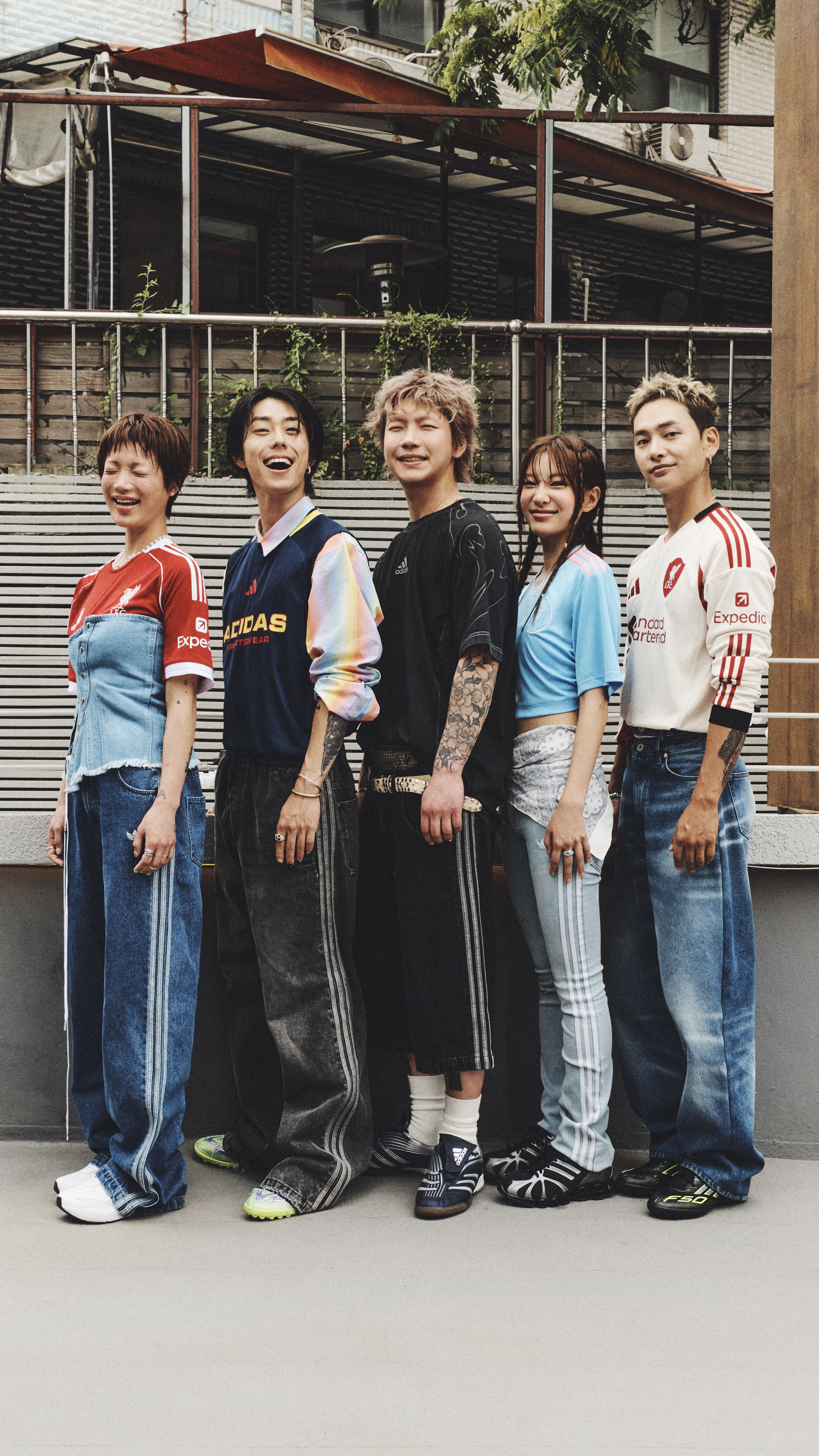 A group of young people, dressed in casual clothing, stand together in front of a building with a corrugated metal facade.