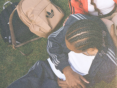 Bilden visar en person som bär en beige ryggsäck och en svartvit randig mössa, sittande på gräset med andra ryggsäckar i bakgrunden.