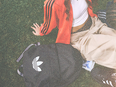 Bilden visar en person som bär en orange jacka och svarta byxor, stående på en gräsbevuxen plan.