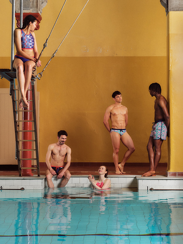 Un grupo de hombres sin camisa están de pie y sentados en una piscina, con una mujer sentada en un trampolín en primer plano.