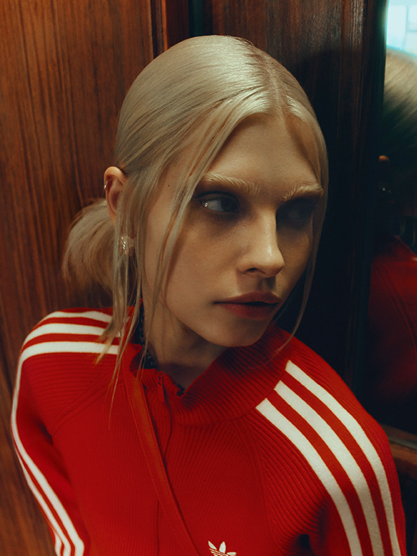 En blond kvinde iført en rød og hvid stribet jakke står foran en træbaggrund.