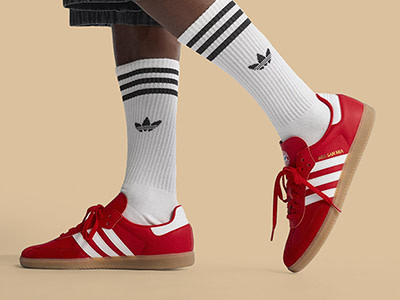 Unas zapatillas adidas rojas con calcetines blancos y rayas negras sobre un fondo beige.