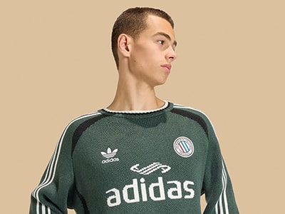 Un hombre joven con una camiseta verde de adidas sobre un fondo beige.