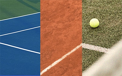 En tennisplan med en blå hårda underlag, en orange grusplan och en grön konstgräs yta, med en tennisboll synlig på gräset.
