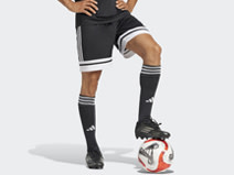 A person wearing black athletic shorts and socks, standing on a soccer ball against a plain white background.