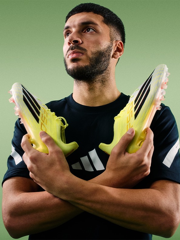 A man wearing a black sports jersey stands with his arms crossed, holding yellow sports equipment against a green background.