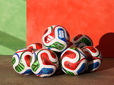 Un montón de balones de fútbol estampados se asientan sobre una superficie marrón, con un fondo verde y rojo vibrante.