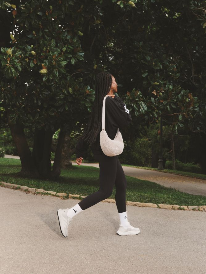 A person in black athletic clothing is walking on a path surrounded by lush greenery and trees.
