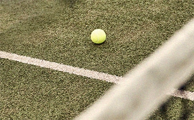 En klargul tennisboll vilar på en prunkande grön konstgräsplan, med en vit gränslinje synlig i förgrunden.