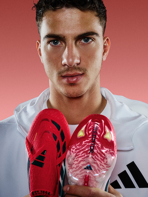A young man wearing a white shirt and holding a pair of red boxing gloves stands against a red background.