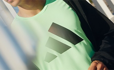 A person wearing a mint green shirt with geometric shapes on the sleeve, standing in front of a white background.
