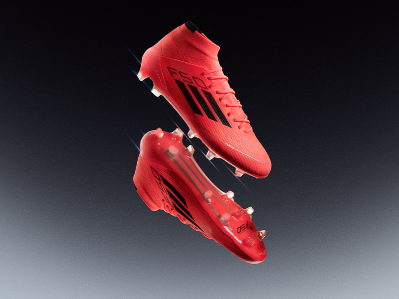 Un par de botas de fútbol o botas de fútbol rojas brillantes se suspenden en el aire sobre un fondo oscuro.