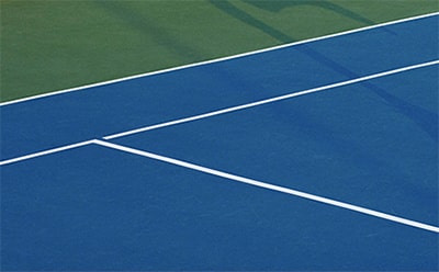 Bilden föreställer en tennisplan med blå spelyta och vita gränslinjer mot en grön bakgrund.