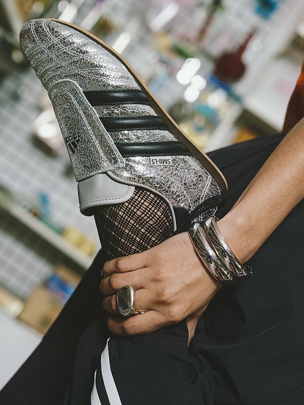 A close-up view of a person's hand wearing a silver and black athletic shoe, with a blurred background of what appears to be a retail store or display.