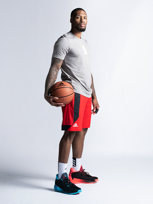 A young man in a gray t-shirt and red shorts stands holding a basketball, with a plain white background.