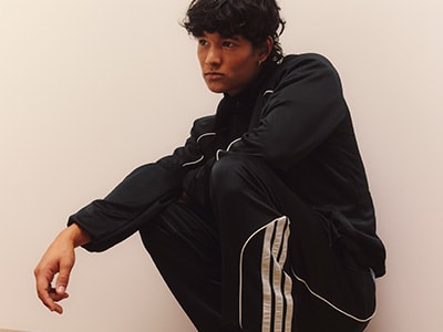 A person wearing a black jacket is sitting in a plain, light-colored room.
