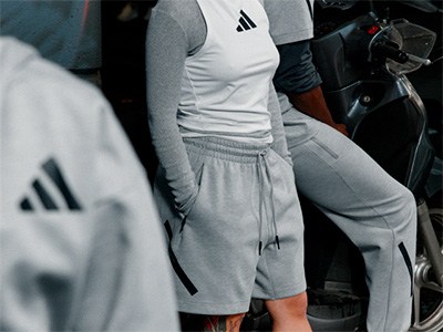 The image shows a person wearing a white Adidas shirt and gray sweatpants, standing in front of a dark background.