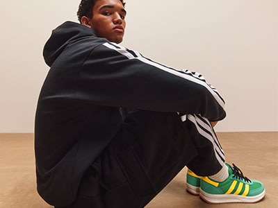 A person wearing a black suit and green and white sneakers is sitting on the floor in a plain room.