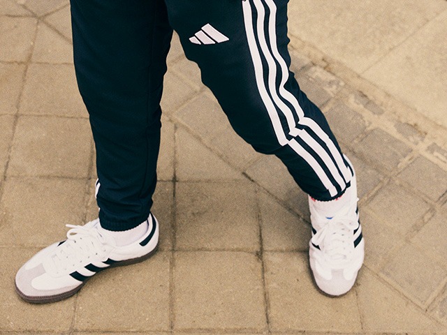 The image shows a person's lower body wearing black and white athletic pants and shoes, standing on a tiled floor.