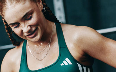 A woman with braided hair wearing a green athletic top, smiling and looking directly at the camera against a dark background.