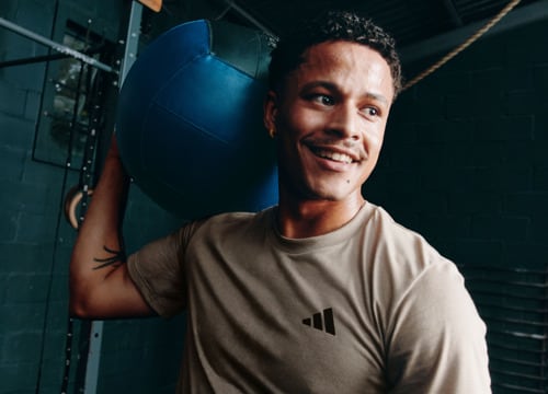 A smiling man wearing a beige t-shirt stands in front of a blue background.