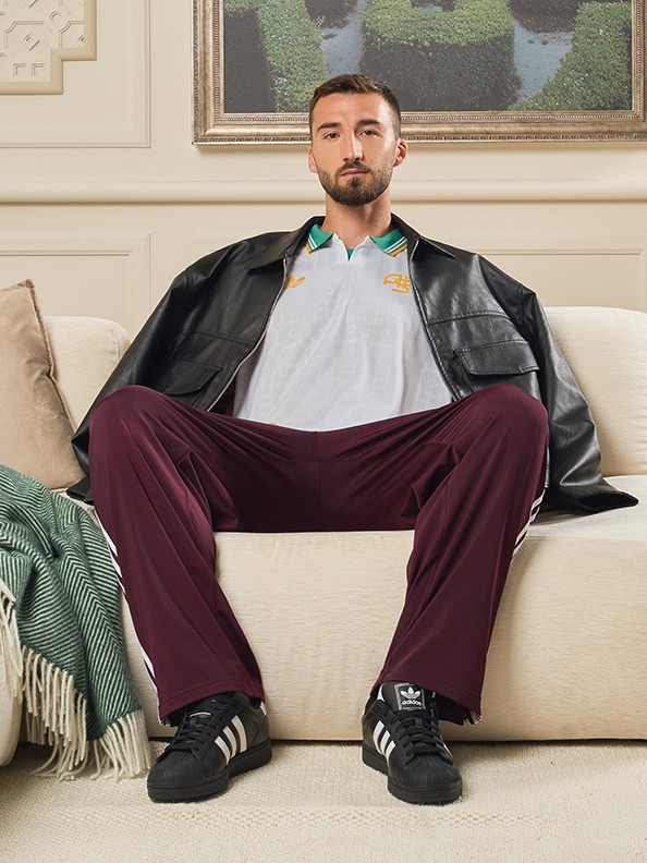 Un uomo con la barba e l'abbigliamento casual si siede comodamente su un divano, circondato da elementi decorativi e un paesaggio incorniciato sullo sfondo.