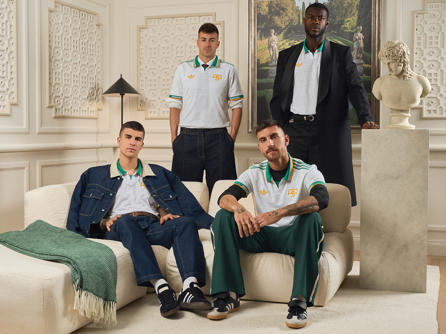 The image features four individuals wearing matching green and white uniforms, seated on a couch in an ornate, white-walled room with decorative architectural elements and a statue in the background.