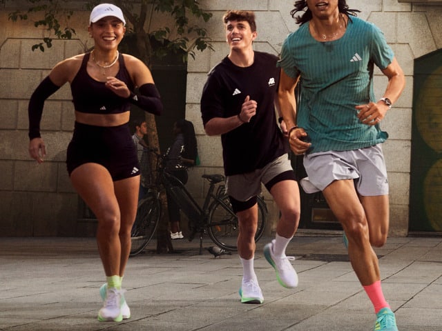 Three people, two women and one man, are jogging together on a paved path surrounded by plants and a brick wall in the background.