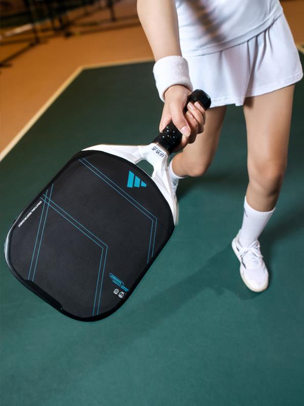 A person in athletic attire is holding a black and blue racket bag on a green court.