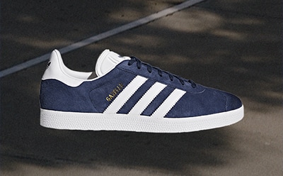 Le sneaker adidas Gazelle blu navy e bianche risaltano su uno sfondo scuro, con ombre e dettagli che creano un effetto d'effetto.