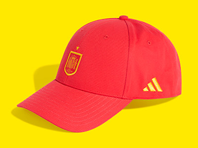 La gorra de béisbol roja con el logotipo de la selección española y el logotipo de adidas destaca sobre un vibrante fondo amarillo.