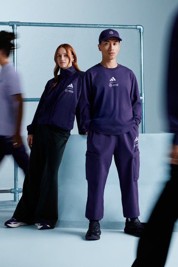 Dos personas con ropa deportiva de adidas se encuentran en un estudio con un fondo azul y estructuras metálicas visibles.