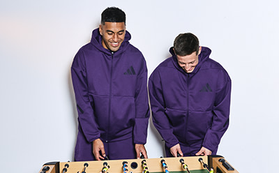 Two individuals wearing matching purple hooded sweatshirts stand on a platform against a plain white background.